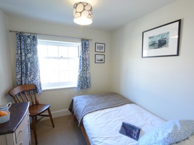 A small bedroom with a single bed a wooden chair a chest of drawers and three framed pictures at Pebble Beach Cottage Aldeburgh