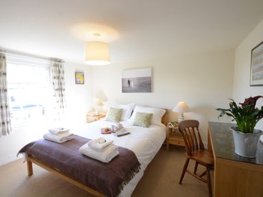 A bedroom with a double bed with towels on a blanket and a wooden chair at Pebble Beach Cottage in Aldeburgh