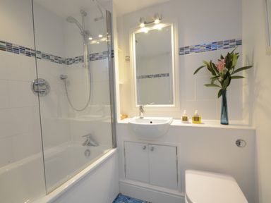 A bathroom with a bathtub shower combination a sink a mirror and a vase with flowers at Pied a Mer Aldeburgh in Aldeburgh