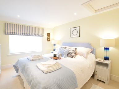 A bedroom with a double bed blue bedspread pillows bedside tables lamps and a window with striped blinds at Pied a Mer Aldeburgh