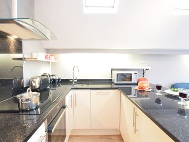 A kitchen with black countertops a stove with a pot a toaster a microwave and food on the counter at Pied a Mer Aldeburgh