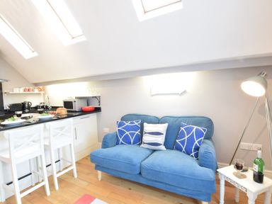 A small kitchen and seating area with a blue sofa and white chairs at Pied a Mer Aldeburgh