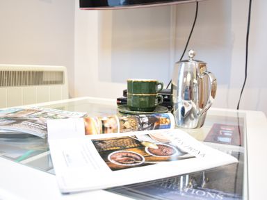 A glass table with a magazine a silver coffee pot and two green coffee cups at Pied a Mer Aldeburgh