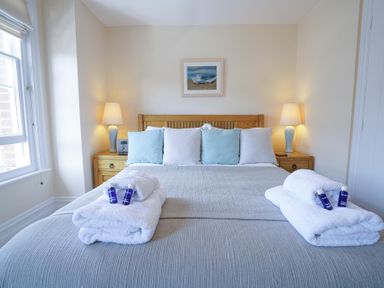 A bedroom with a double bed with blue and white pillows bedside tables with lamps and folded towels at The Hideaway in Aldeburgh