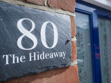 A house number plaque with 80 The Hideaway on a brick wall near a blue door at The Hideaway Aldeburgh