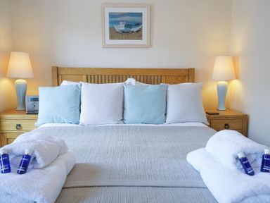 A bedroom with a wooden bed frame and five pillows with nightstands and lamps on both sides at The Hideaway, Aldeburgh