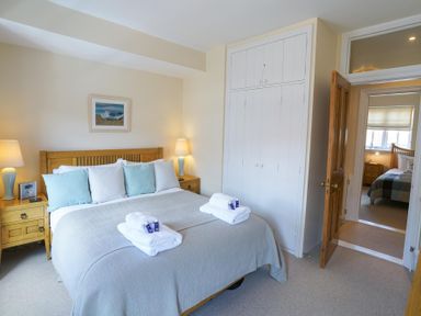 A bedroom with a double bed, bedside tables with lamps, a painting on the wall, and an open door leading to another bedroom at The Hideaway in Aldeburgh