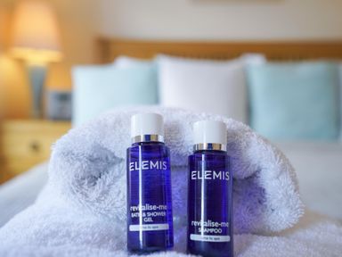 Two small blue bottles of Elemis bath and shower gel and shampoo on a white towel in a bedroom at The Hideaway in Aldeburgh
