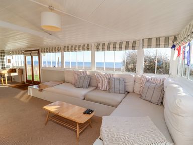 A living room with a sectional sofa striped cushions a wooden coffee table and large windows showing a sea view at Valetta Thorpeness in Thorpeness