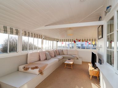 A sunroom with a large corner sofa and striped cushions a small wooden table and a TV on a wooden stand at Valetta Thorpeness in Thorpeness