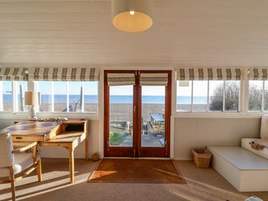 A room with a wooden desk and chair near windows overlooking a beach at Valetta Thorpeness in Thorpeness