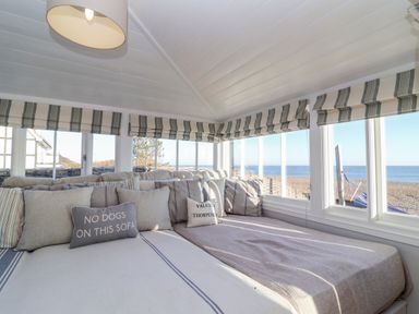 A corner seating area with cushions and a large window showing a beach view at Valetta Thorpeness in Thorpeness