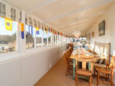 A dining area with a long wooden table set with plates and glasses surrounded by wooden chairs and a bench at Valetta Thorpeness in Thorpeness