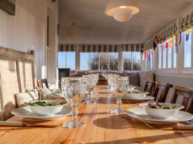 A dining table set with glassware bowls of salad and plates in a room with large windows and wooden chairs at Valetta Thorpeness in Thorpeness
