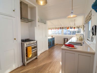 A kitchen with a stove, a sink, a countertop with peppers on a plate, a blue cabinet under windows with nautical flags at Valetta, Thorpeness in Thorpeness