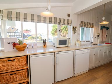 A kitchen counter with a bread box a fruit bowl a microwave a knife block a kettle and cupboards below at Valetta Thorpeness in Thorpeness