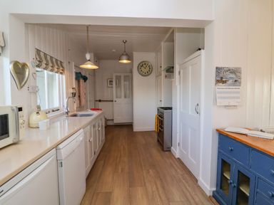 A kitchen with wooden floor white cabinets a sink microwave kettle stove and blue cupboard at Valetta Thorpeness in Thorpeness