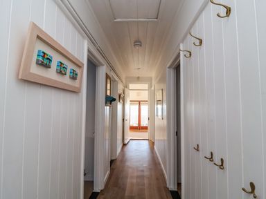 A hallway with wooden floor and white paneled walls decorated with hooks and framed artwork at Valetta Thorpeness in Thorpeness
