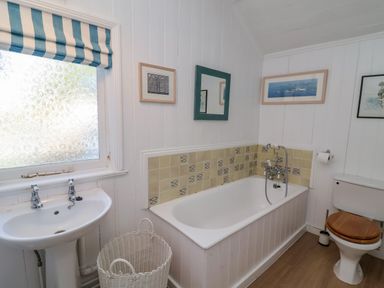 A bathroom with a bathtub sink toilet wicker basket and framed pictures on white paneled walls at Valetta Thorpeness in Thorpeness