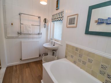 A bathroom with a bathtub a sink a towel rack and a window at Valetta Thorpeness in Thorpeness