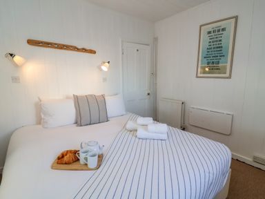 A bedroom with a bed with white and striped linens a wooden tray with cups and croissants and framed artwork on the wall at Valetta Thorpeness in Thorpeness