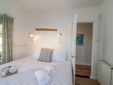 A bedroom with a bed striped blanket and rolled towels next to a window with striped curtains at Valetta Thorpeness in Thorpeness