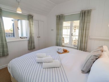 A bedroom with a striped bedspread towels on the bed and windows with curtains at Valetta Thorpeness in Thorpeness