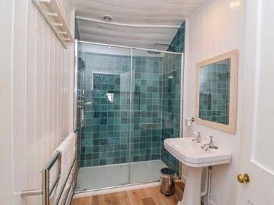 A bathroom with a walk-in shower with green tiles a white sink and a mirror at Valetta Thorpeness in Thorpeness
