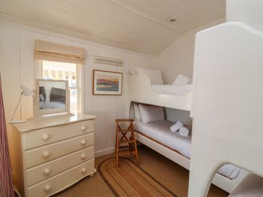 A small bedroom with white bunk beds a wooden chest of drawers a mirror and a woven rug at Valetta Thorpeness in Thorpeness