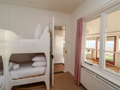 A small bedroom with white bunk beds and a window looking out to a patio and the sea at Valetta Thorpeness in Thorpeness