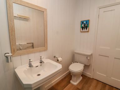 A bathroom with a pedestal sink and mirror and a toilet with a small painting on the wall at Valetta Thorpeness in Thorpeness