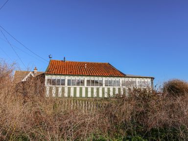 A house with a red tiled roof and a glass enclosed porch surrounded by bushes at Valetta Thorpeness in Thorpeness
