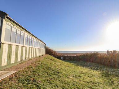 A grassy yard with a building on the left and a beach with ocean in the background at Valetta Thorpeness in Thorpeness