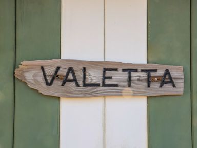 A wooden sign with the word Valetta mounted on a green and white striped door at Valetta Thorpeness