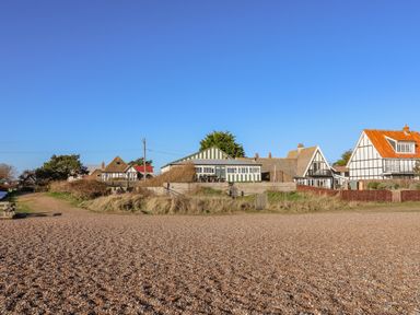 A row of houses behind a grassy area and pebble beach at Valetta Thorpeness
