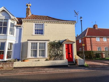 A two-story cream brick house with a red front door and windows near the street at Winkle Cottage Aldeburgh