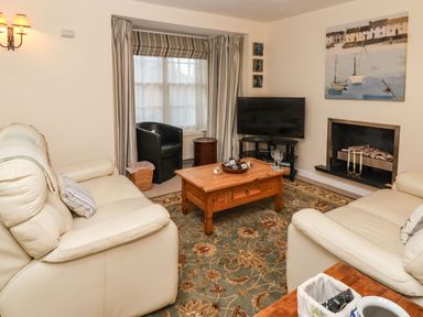 A living room with cream leather sofas a wooden coffee table a television near a fireplace and striped curtains at Winkle Cottage in Aldeburgh