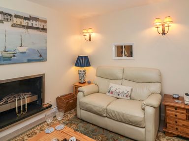 A living room with a cream leather sofa a wooden coffee table a fireplace and a painting above at Winkle Cottage Aldeburgh