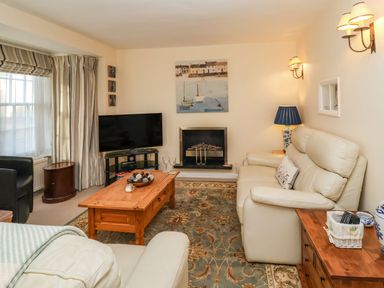 A living room with cream sofas coffee table television and fireplace at Winkle Cottage Aldeburgh