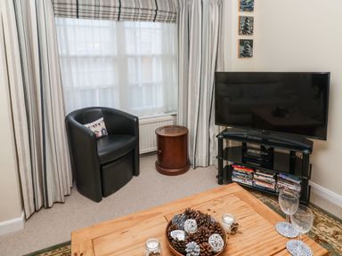 A living room corner with a black chair a wooden side table a television on a stand and a wooden coffee table with pinecones and candles at Winkle Cottage Aldeburgh