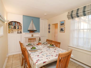 A dining room with a wooden table and chairs set for four meals with a sailboat model on a shelf at Winkle Cottage Aldeburgh