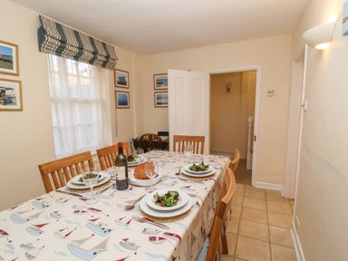 A dining room with a table set for four with salad plates wine glass and a bottle of wine at Winkle Cottage Aldeburgh