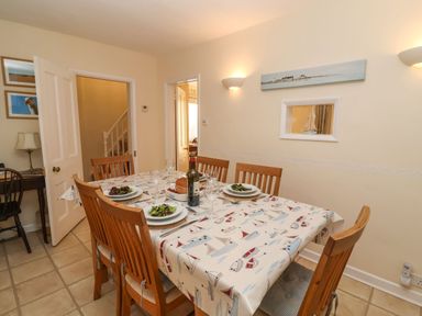 A dining room with a table set for six with plates of salad and a wine bottle at Winkle Cottage Aldeburgh