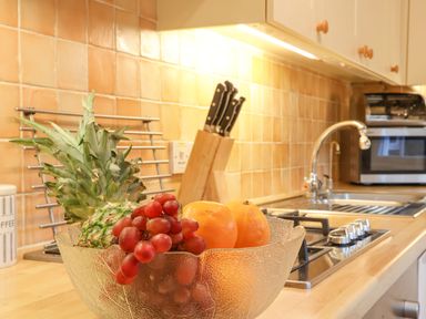 A kitchen countertop with a glass bowl of fruit next to a gas stove and a sink at Winkle Cottage Aldeburgh