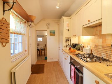 A kitchen with white cabinets wooden countertop gas stove and a window with floral blind at Winkle Cottage Aldeburgh