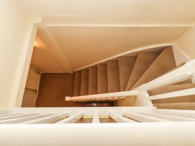 A staircase with beige carpet and white railing at Winkle Cottage Aldeburgh