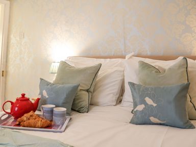A bed with pillows and a tray holding a red teapot croissants and two cups at Winkle Cottage Aldeburgh