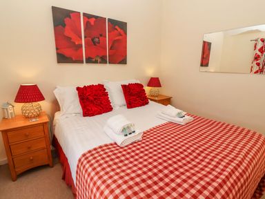 A bedroom with a large bed and red checkered bedspread at Winkle Cottage Aldeburgh