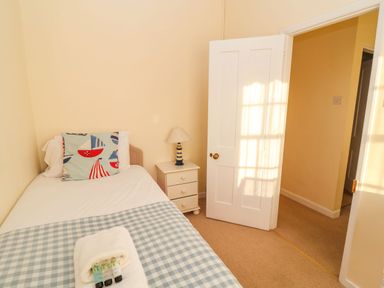 A small bedroom with a single bed a side table with a lamp and an open door at Winkle Cottage Aldeburgh