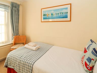 A single bed with folded towels and a patterned pillow next to a window with curtains and a wooden chair at Winkle Cottage Aldeburgh